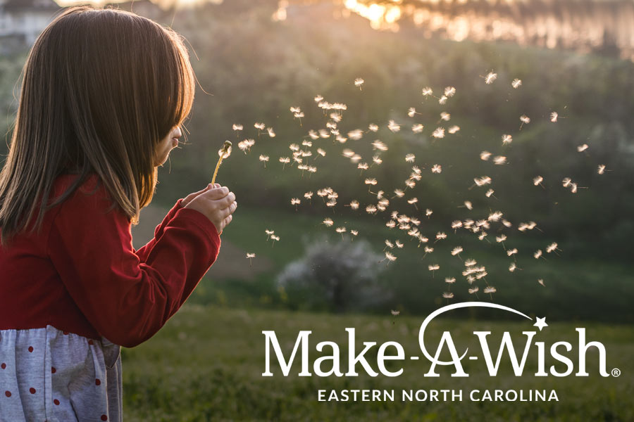 Photo of a little girl blowing on a dandelion at sunset